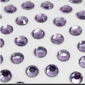 May include: A close-up of a white surface covered in small, round, purple rhinestones.