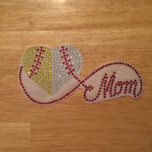 May include: A white heart-shaped iron-on patch with red, yellow, and clear rhinestones. The word "Mom" is spelled out in red rhinestones on a white iron-on patch.