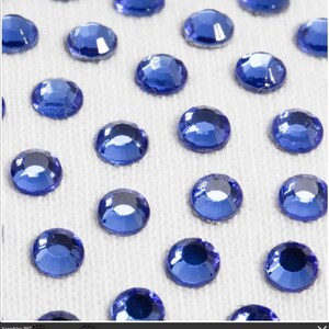 May include: Close-up of a white surface covered with small, round, blue rhinestones.