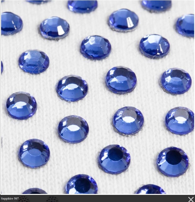 May include: Close-up of a white surface covered with small, round, blue rhinestones.