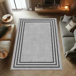 May include: A grey area rug with a black border. The border has three black lines.