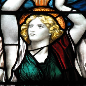 May include: Stained glass window showing a figure with blonde hair, wearing a green and red garment, and a golden halo. The figure's arms are raised, with blue and orange hues in the background.
