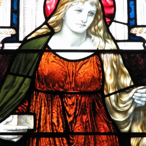 May include: A stained glass window depicting a woman with long blonde hair wearing a red crown and a long orange dress with a floral pattern.