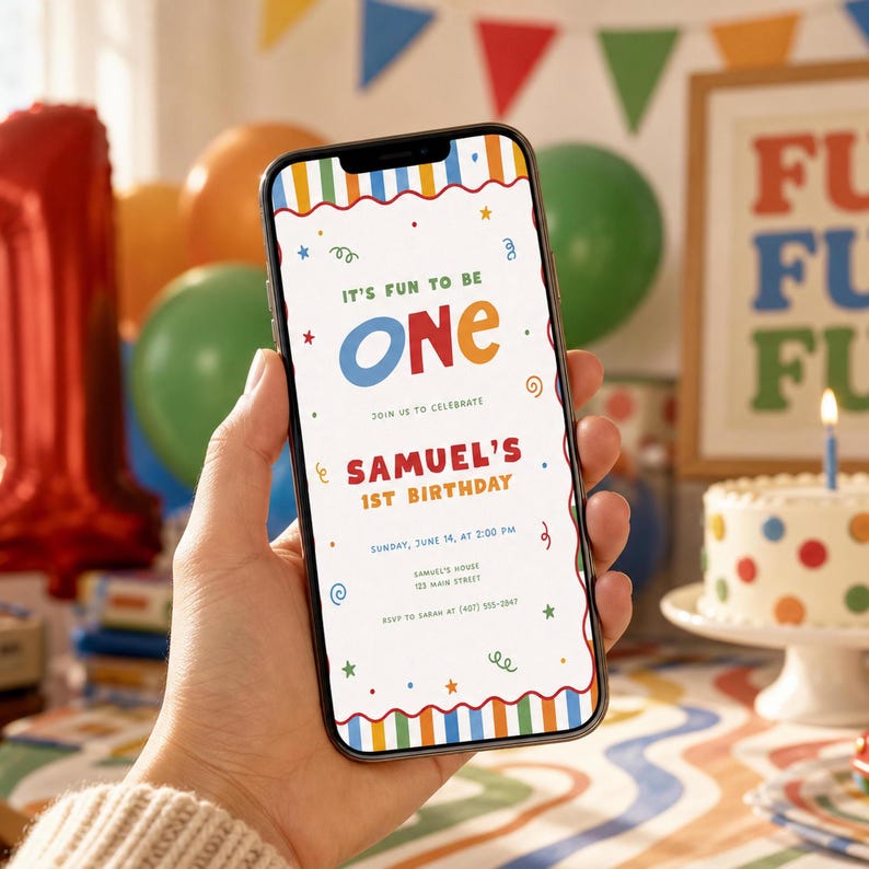 May include: A smartphone displays a colorful birthday invitation with the text "It's Fun to Be One" and "Samuel's 1st Birthday." The design includes stars, swirls, and a striped border. A cake with a lit candle and balloons are in the background.
