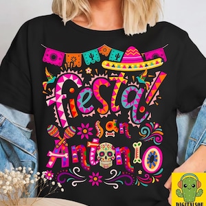May include: Black t-shirt with a colorful "Fiesta en Antonio" graphic. The design includes a sombrero, maracas, a sugar skull, and decorative banners. The text is in a vibrant, multi-colored font, perfect for a festive occasion.