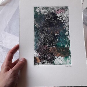 Könnte beinhalten: Abstrakter Kunstdruck auf weißem Papier. Das Kunstwerk zeigt ein strukturiertes Design mit dunkelgrünen, schwarzen und rosa Farbtönen. Der Druck wird von einer Hand gehalten, die die Kanten des Papiers zeigt. Der Druck ist signiert und nummeriert.