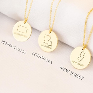 May include: Three gold necklaces with state-shaped pendants. The pendants are engraved with the state names: Pennsylvania, Louisiana, and New Jersey.
