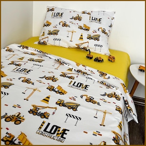 Könnte beinhalten: Weiß-gelbes Bettwäsche-Set zum Thema Bau. Das Set enthält einen Kissenbezug und einen Bettbezug, beide mit Illustrationen von Baufahrzeugen, Kränen und dem Text "I LOVE CONSTRUCTION". Das Spannbetttuch ist einfarbig gelb.