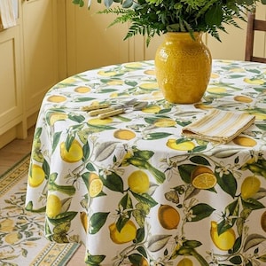 May include: A round white tablecloth featuring a lemon and leaf design. A yellow vase with green foliage is on the table. A folded napkin and cutlery are also present. A matching rug is visible in the corner.