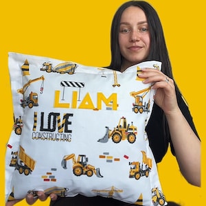 Puede incluir: Funda de almohada blanca con temática de construcción. La funda de almohada presenta vehículos de construcción amarillos, el nombre "LIAM" en letras amarillas y la frase "I LOVE CONSTRUCTING". El fondo es amarillo brillante.