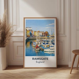 Puede incluir: Un póster enmarcado que muestra una escena del puerto de Ramsgate, Inglaterra. La imagen presenta numerosos barcos atracados en el agua azul, con edificios coloridos a lo largo de la costa bajo un cielo despejado. El póster tiene un marco de madera y el texto "RAMSGATE England" en la parte inferior.