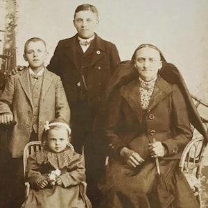 May include: Vintage sepia-toned photograph of a family posing for a portrait. The image features a woman seated with an umbrella, a young child seated in a chair, and two young men standing behind them. The photograph is mounted on a card.