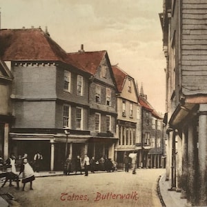 May include: A vintage postcard depicting a street scene in Totnes, Butterwalk. The image shows multi-story buildings with brown roofs, a covered walkway with columns, and pedestrians walking along the road. The text Totnes, Butterwalk is visible.