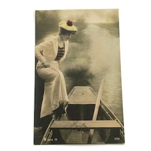 Carte postale photo ancienne - Femme embarquant dans un canoë vêtue d'un haut à rayures et d'un chapeau bateau - RPPC française teintée à la main