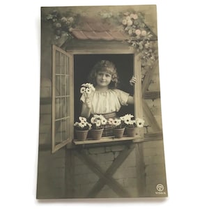 Vintage ansichtkaart – Meisje met madeliefjes voor het raam van de cottage – begin jaren 1900