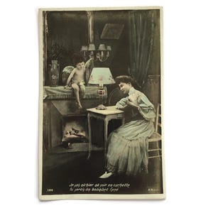 Antieke Franse ansichtkaart – Romantische scène met schrijvende vrouw en Cupido bij het vuur | Handgekleurde fantasiekaart, begin jaren 1900