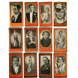 Op de afbeelding: Een verzameling vintage celebrity-ruilkaarten. Elke kaart toont een zwart-wit portret van een persoon, tegen een rode achtergrond met gouden rand. De kaarten tonen namen als Beniamino Gigli en Zarah Leander.