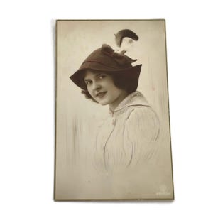 Stara pocztówka fotograficzna – olśniewająca kobieta w kapeluszu z piór, portret z początku lat 1900.