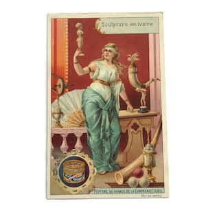 May include: A vintage advertisement card depicting a woman in classical dress holding an ivory sculpture. The card has a red backdrop and the text "Sculpture en ivoire." Other elements include a fan, a horn, and a can of Peptone de Viande.