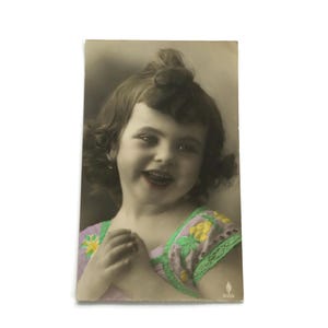 Postal antigua coloreada a mano: Niña sonriente con vestido floral, principios del siglo XX, RPPC, sin usar.