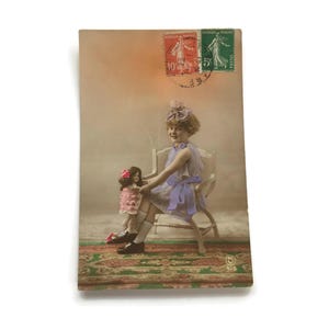 Vintage Franse ansichtkaart met pop – handgekleurde meisjesfoto uit de jaren 1920 – art-decotijdperk – RPPC-scène met vloerkleed en stoel