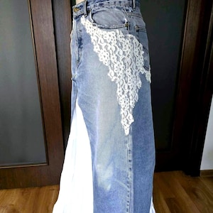 May include: A denim skirt with a white lace overlay on the front. The skirt has a high waist and a front slit, revealing white fabric. The skirt is displayed on a mannequin.