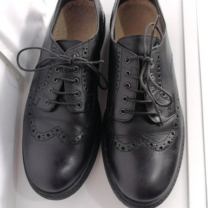 May include: A pair of black leather brogue shoes with lace-up closures. The shoes have a decorative pattern of small holes around the toe.