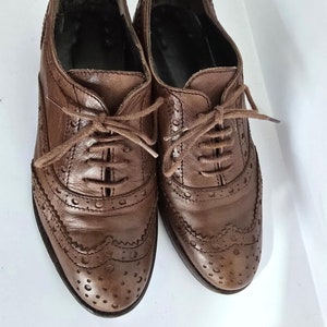 May include: A pair of brown leather lace-up shoes with a brogue design. The shoes have a rounded toe and a low heel.