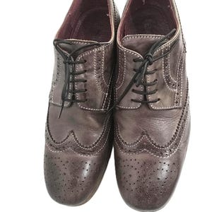 May include: A pair of brown leather brogue shoes with a lace-up closure. The shoes have a wingtip design and a perforated pattern.