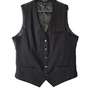 Könnte beinhalten: Eine schwarze Weste mit einer fünf-Knopf-Vorderseite, einer Brusttasche und zwei unteren Leistentaschen. Das Kleidungsstück hat einen V-Ausschnitt, ein glattes Innenfutter und wird auf einem schwarzen Kunststoffbügel vor weißem Hintergrund präsentiert.