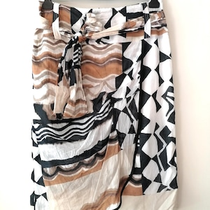 May include: A knee-length wrap skirt featuring a multi-panel design with a mix of black, white, and tan patterns. The skirt includes a tie-waist belt, belt loops, and a combination of geometric shapes and wavy horizontal lines across the fabric.