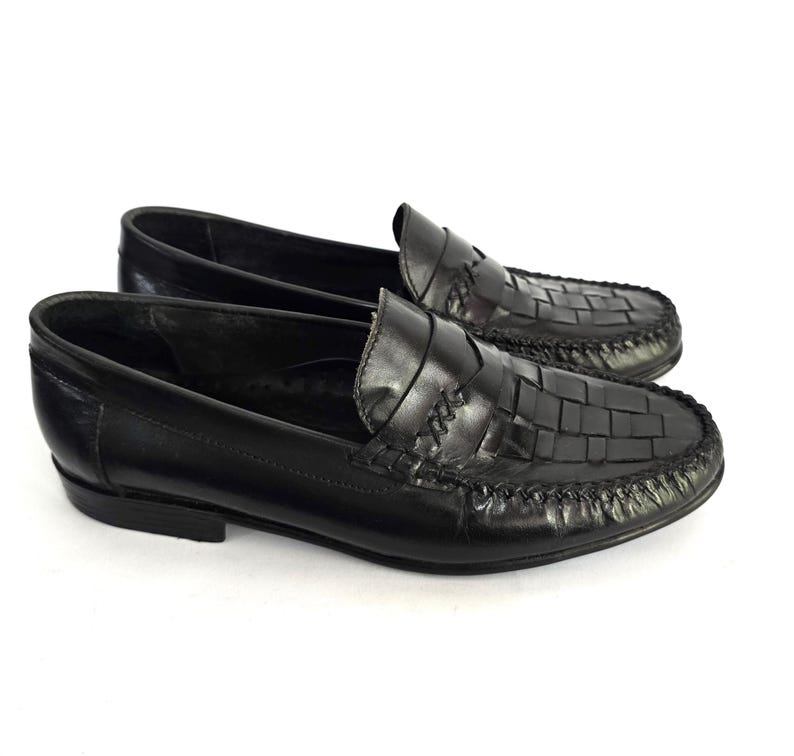 May include: Black leather loafers with a woven pattern on the toe and a single strap across the top.