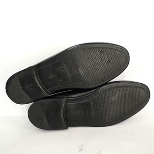 May include: A pair of black leather shoes with a textured sole. The shoes are laid flat on a white surface.