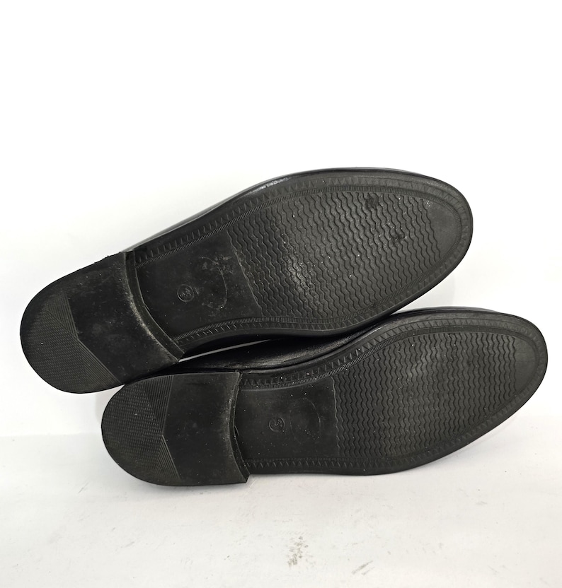 May include: A pair of black leather shoes with a textured sole. The shoes are laid flat on a white surface.