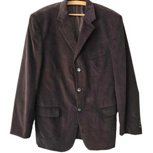 May include: A dark brown corduroy blazer with a single-breasted closure and three buttons. The blazer has a classic fit and features two flap pockets on the front.