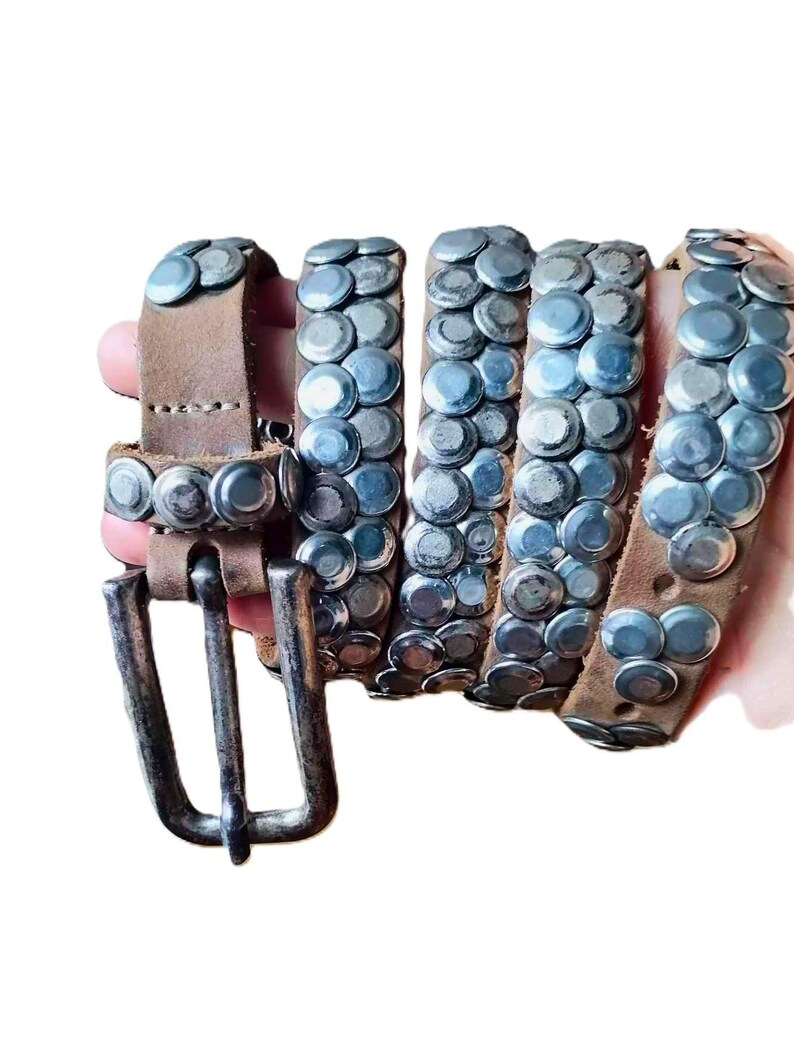 May include: A brown leather belt with silver-colored studs. The belt has a silver buckle and is studded with multiple rows of silver rivets. The belt is shown coiled, with the buckle end visible.
