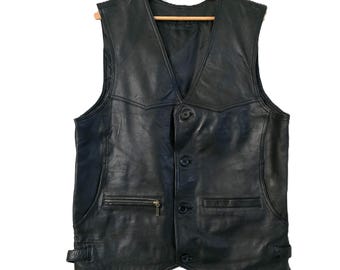 May include: Black leather vest with a V-neck, button closure, and a zippered chest pocket. The vest has two front pockets and adjustable side straps. It is hanging on a wooden hanger.