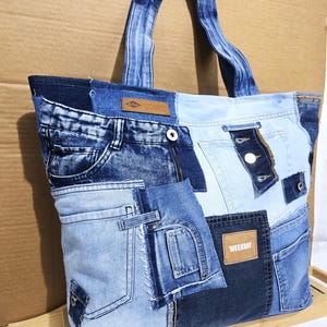 Peut inclure: Un sac fourre-tout en patchwork de denim, composé de différents bleus de jeans. Le sac présente plusieurs poches, fermetures éclair et une étiquette Weekday. Les anses sont en denim.
