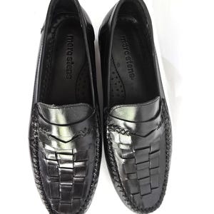 May include: A pair of black leather loafers with a woven design. The loafers have a moc toe and a leather sole. The brand name "marc stevens" is printed on the insole.