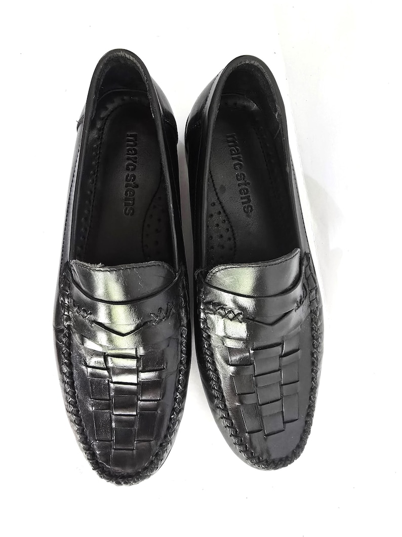 May include: A pair of black leather loafers with a woven design. The loafers have a moc toe and a leather sole. The brand name "marc stevens" is printed on the insole.