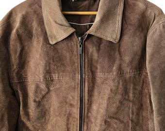Puede incluir: Una chaqueta de ante marrón con cierre de cremallera y dos bolsillos. La chaqueta está colgada en una percha de madera.