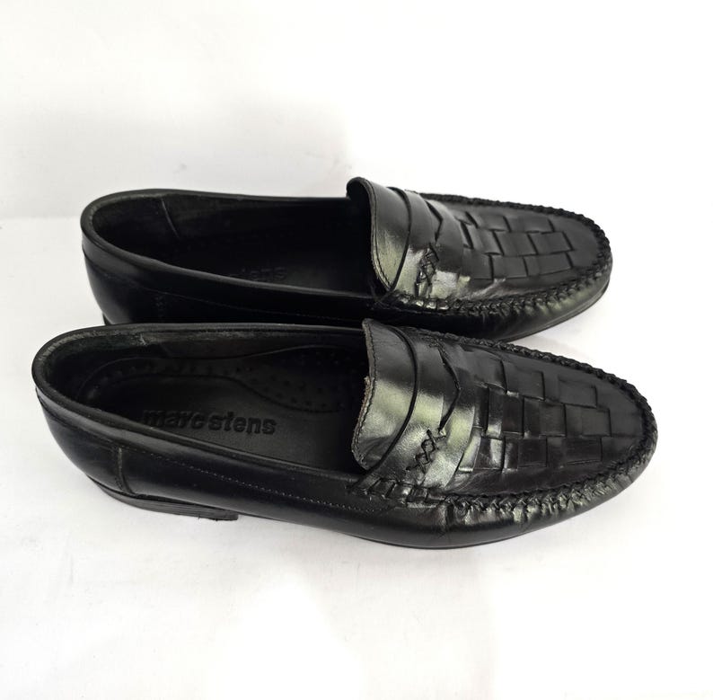 May include: A pair of black leather loafers with a woven pattern. The loafers have a moc toe design and a leather sole. The brand name "Marsten's" is visible on the insole.