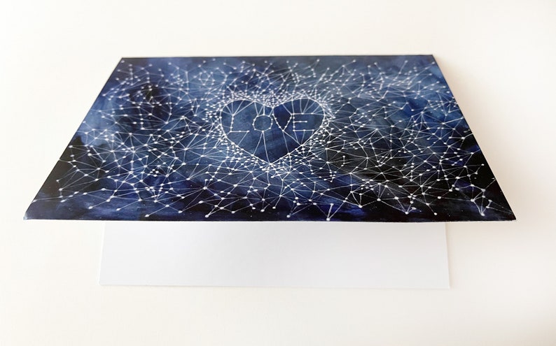 Peut inclure: Une carte bleue et blanche avec un motif de constellation repr&eacute;sentant un c&oelig;ur avec le mot "LOVE" &agrave; l'int&eacute;rieur. La carte est vierge &agrave; l'int&eacute;rieur pour &eacute;crire un message.