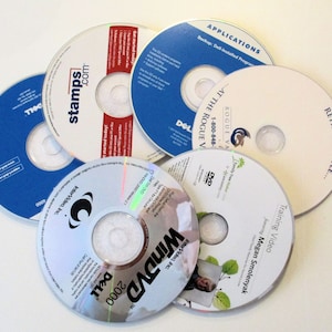 May include: A collection of six silver DVDs with various labels. The labels include text such as "WinDVD", "ROGUE VA", "APPLICATIONS", "RETIRE IN STYLE", "stamps.com", and "Training Video".