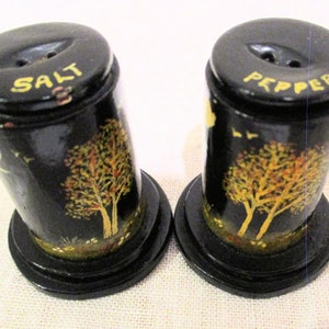 May include: A set of black salt and pepper shakers with gold painted trees and the words "Salt" and "Pepper" on the tops.