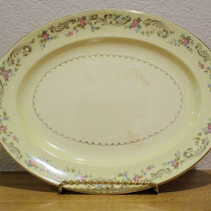 May include: A yellow oval serving platter with a gold rim and a floral design. The flowers are pink, blue, and yellow. The platter has a gold trim around the edge and a gold design in the center.