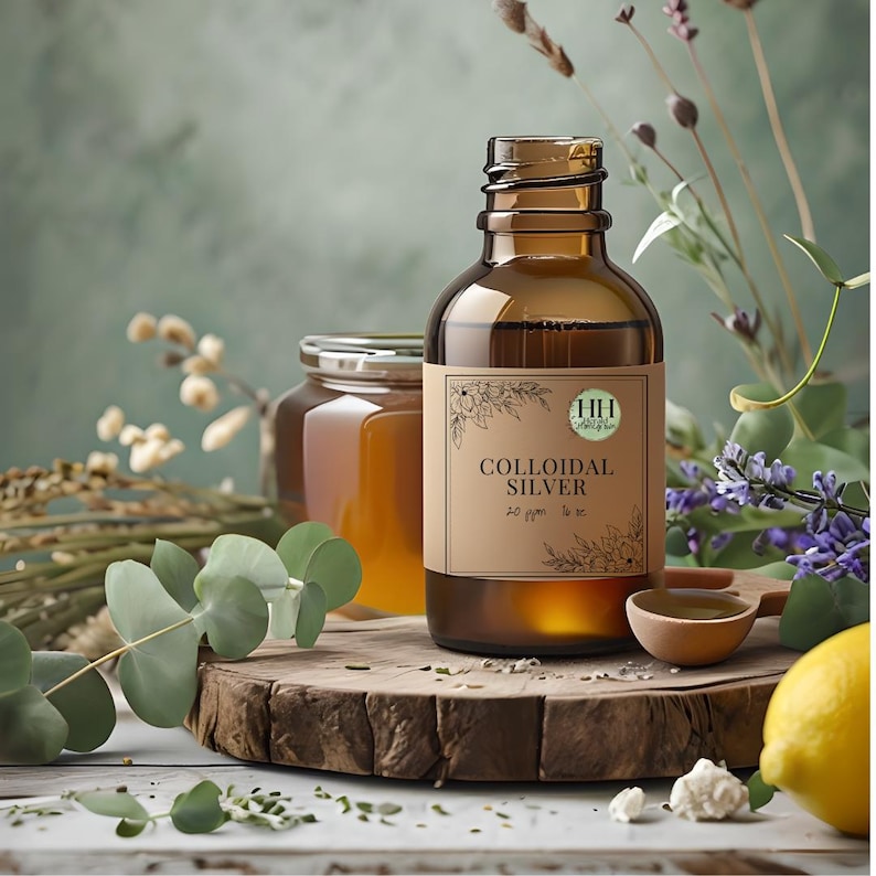 Op de afbeelding: Een bruine glazen fles met het opschrift "Collo&iuml;daal Zilver" met een bloemmotief, op een houten oppervlak. De fles is omgeven door eucalyptusbladeren, lavendel en een pot met amberkleurige vloeistof. Een houten lepel en een citroen zijn ook aanwezig.