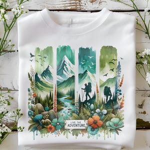 May include: White sweatshirt with a watercolor design of mountains, trees, and a river. The design includes two hikers with backpacks and the text "Live the Adventure".
