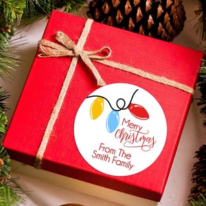 May include: A red gift box with a brown twine bow and a white round sticker with a Christmas lights design. The sticker says "Merry Christmas" and "From The Smith Family".