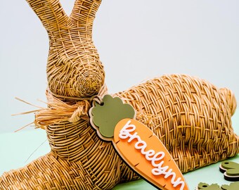 May include: A wicker bunny rabbit with a carrot-shaped tag that says "Braelynn". There are other carrot-shaped tags with names on them, including "Bryce" and "Anna".